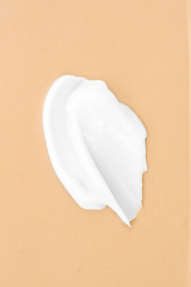 Dollop of white cleansing milk on a peach surface