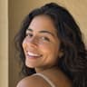 Young woman with long dark curls laughing over her shoulder in a beige tank top